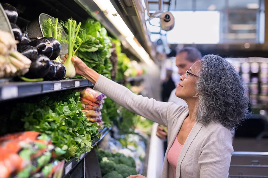 A person selecting fresh vegetables in a grocery store produce aisle, emphasizing healthy food choices and nutrition-focused shopping